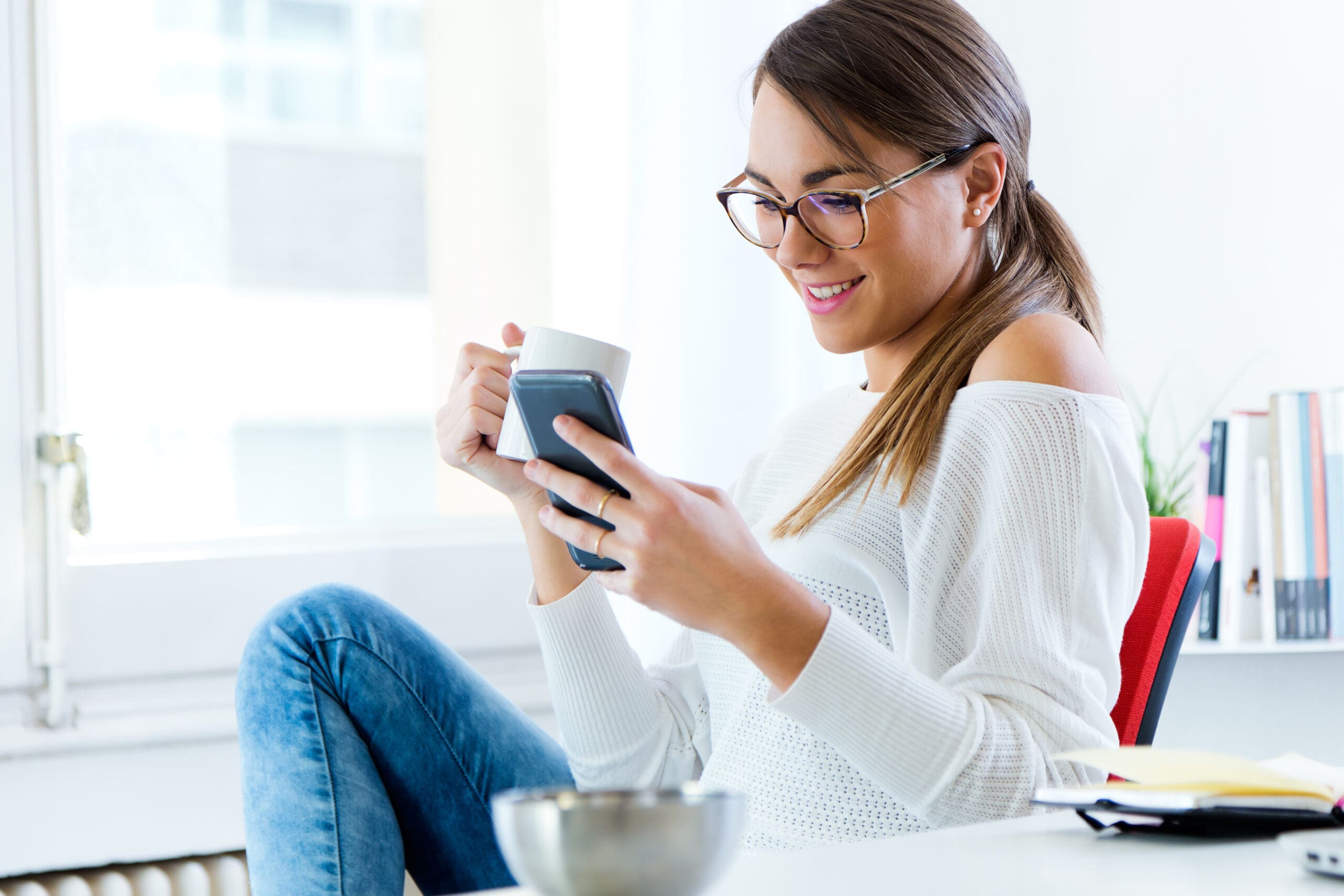 Pretty Young Woman Using Her Mobile Phone In The Office. A woman holding a pregnancy test and a menstrual cycle calendar wondering "How Soon Can I Take a Pregnancy Test?"